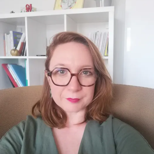 Femme blonde-châtain, avec des yeux verts et des lunettes marrons.