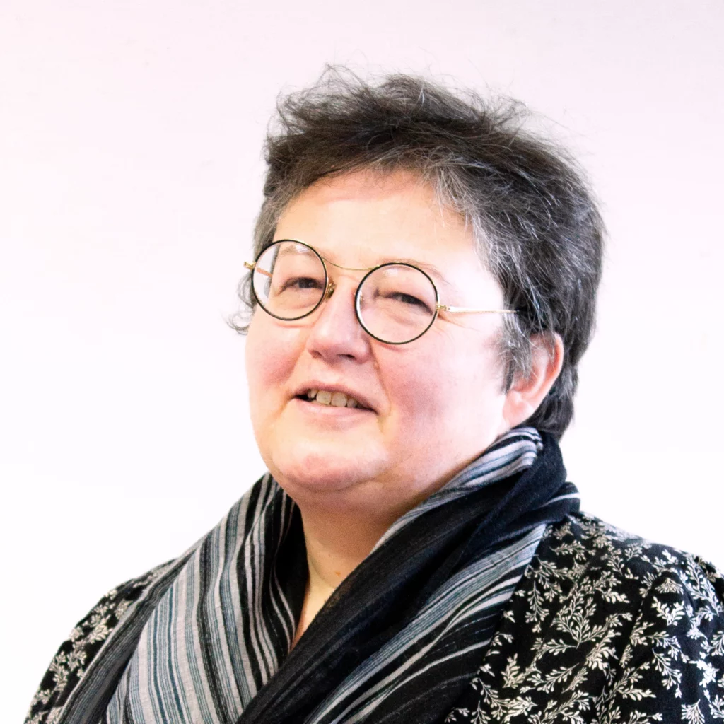 Femme aux cheveux bruns et blancs, aux yeux bleus et lunettes rondes noires.