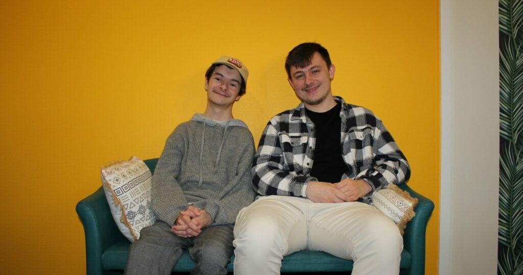 Deux jeunes souriant assis sur un canapé.