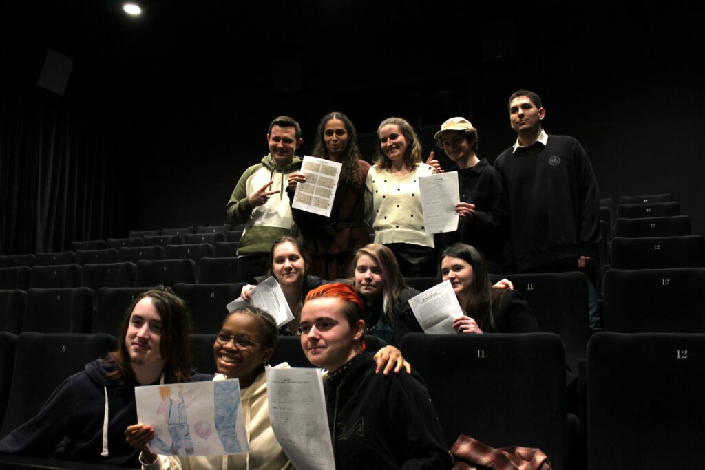 Une douzaine de jeunes souriant dans une salle de cinéma noire, des documents à la main.