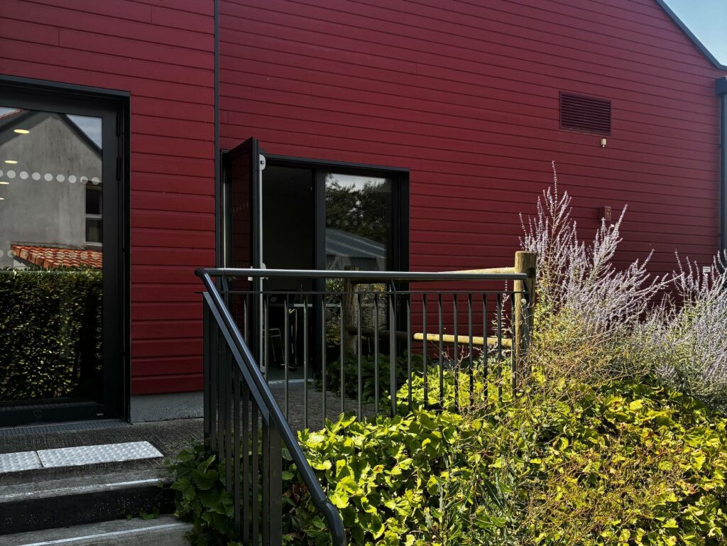 Un bâtiment avec une façade rouge, un escalier et une porte entrouverte.