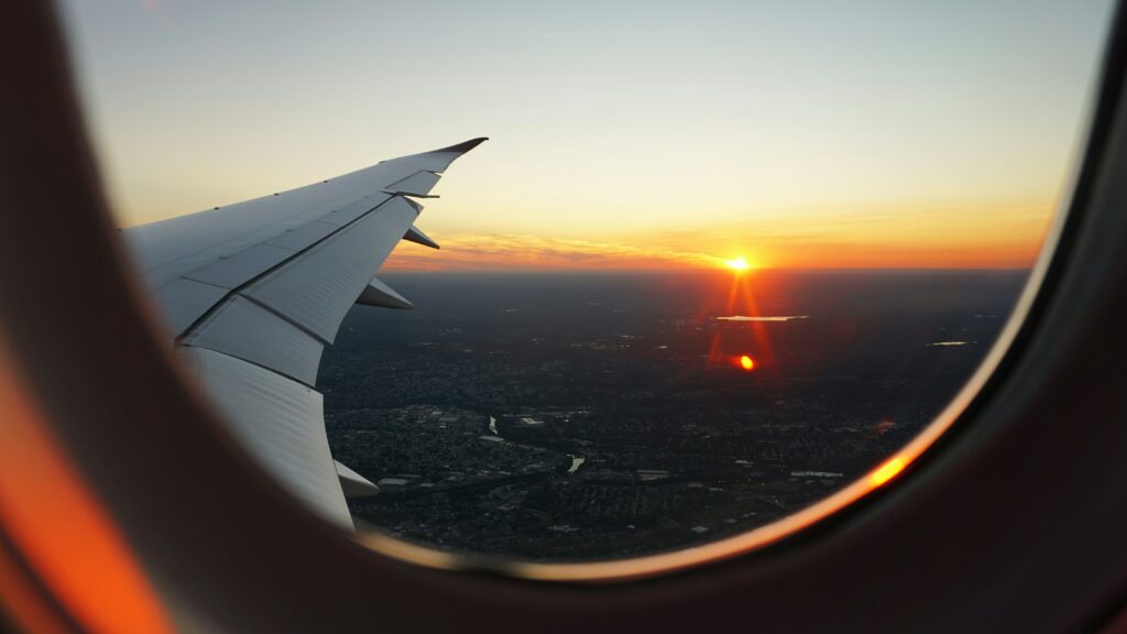 Une aile d'avion dans le ciel devant un coucher de soleil.